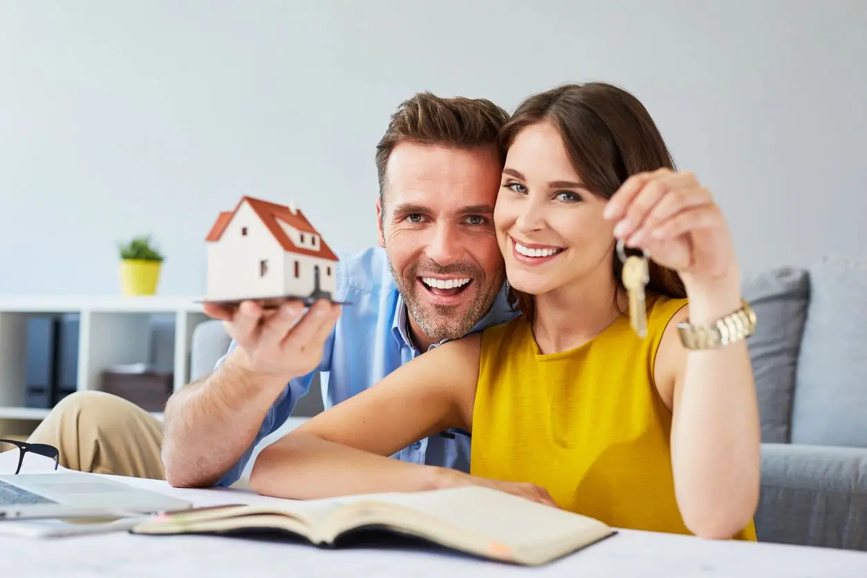 Happy couple holding keys to new home and house miniature, real estate concept